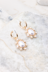 These earrings feature gold hoops, oval pearl dangles with smaller pearl and gold detailing, and a secure post backing.