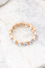 Overhead marble shot of bracelet that features gold hardware, rhinestone details, stretch band, and a slip-on style.
