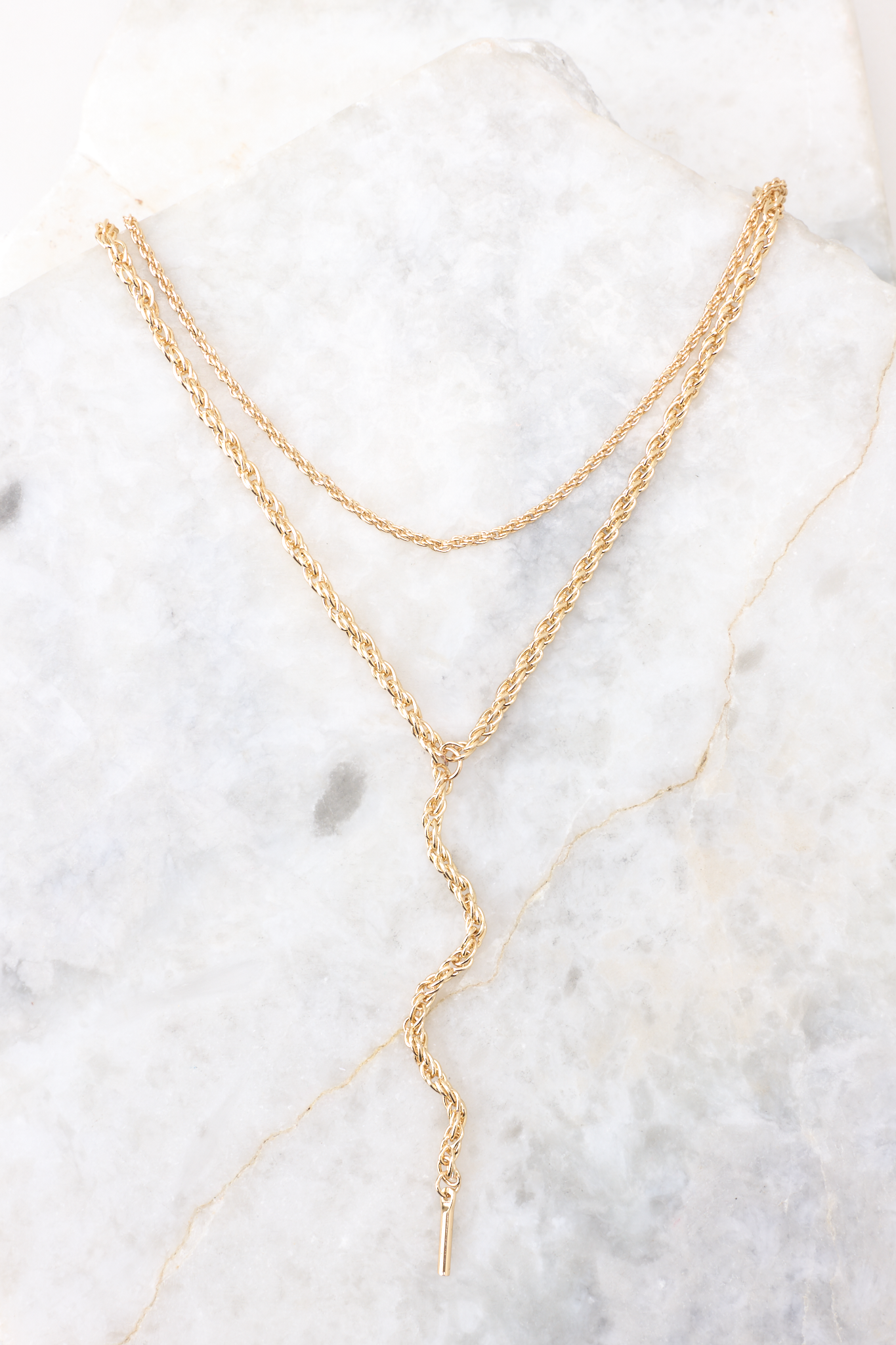 Close up of this necklace stack that features two gold chains with a simple linked design connected by a single lobster-claw clasp. This necklace stack measures 12