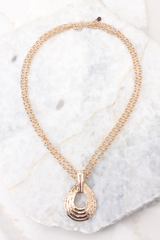 Close up of a necklace featuring a teardrop shaped pendant, a long chain that can be wrapped for a shorter length, and a lobster clasp.
