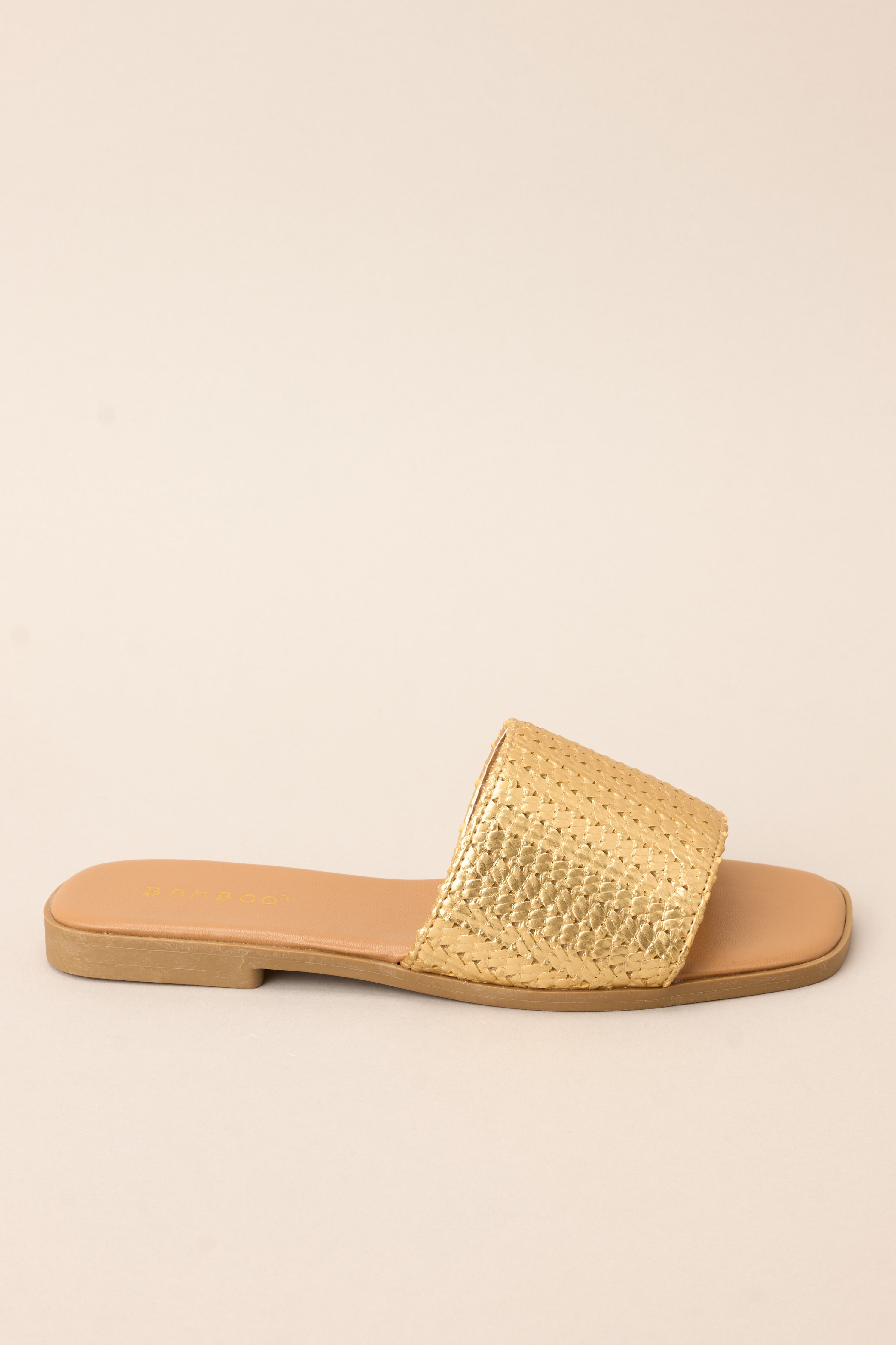 Full side view of these sandals that feature a gold detailed strap over the foot and a slip-on style. 