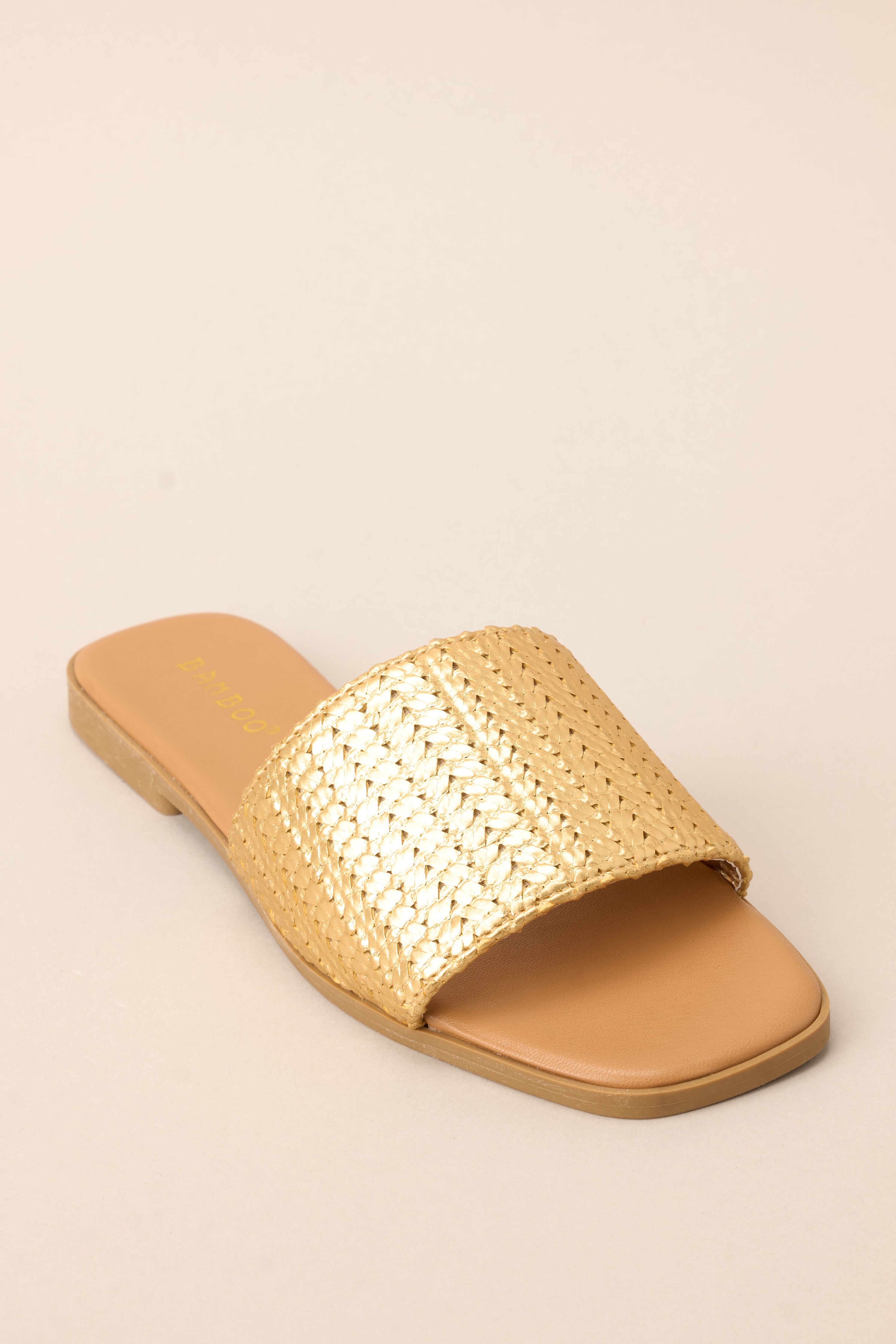 Angled front view of these sandals that feature a gold detailed strap over the foot and a slip-on style.