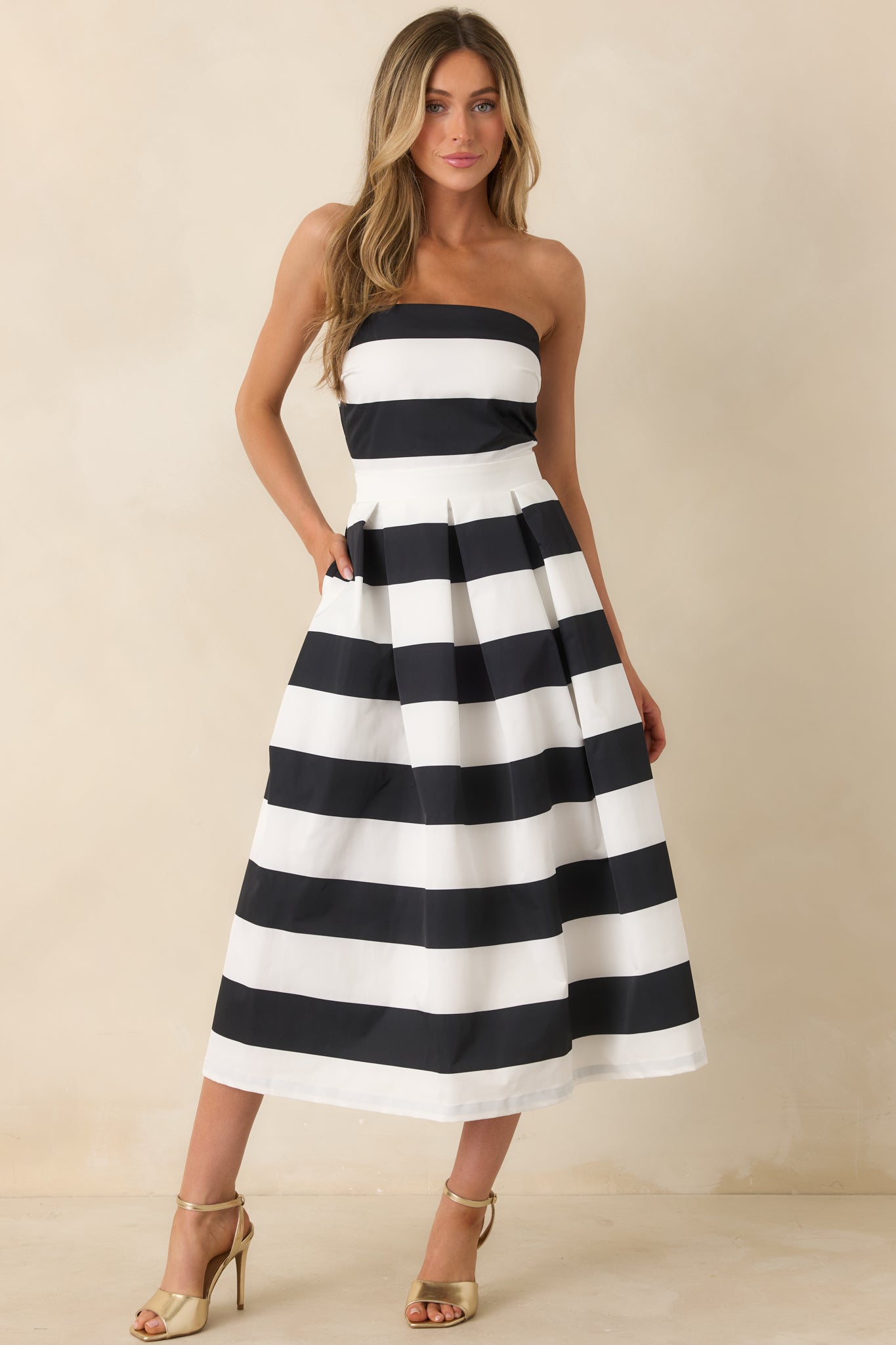 Full-length view of a model wearing the dress, emphasizing the strapless neckline, thick waistband, functional hip pockets, and the timeless stripe pattern