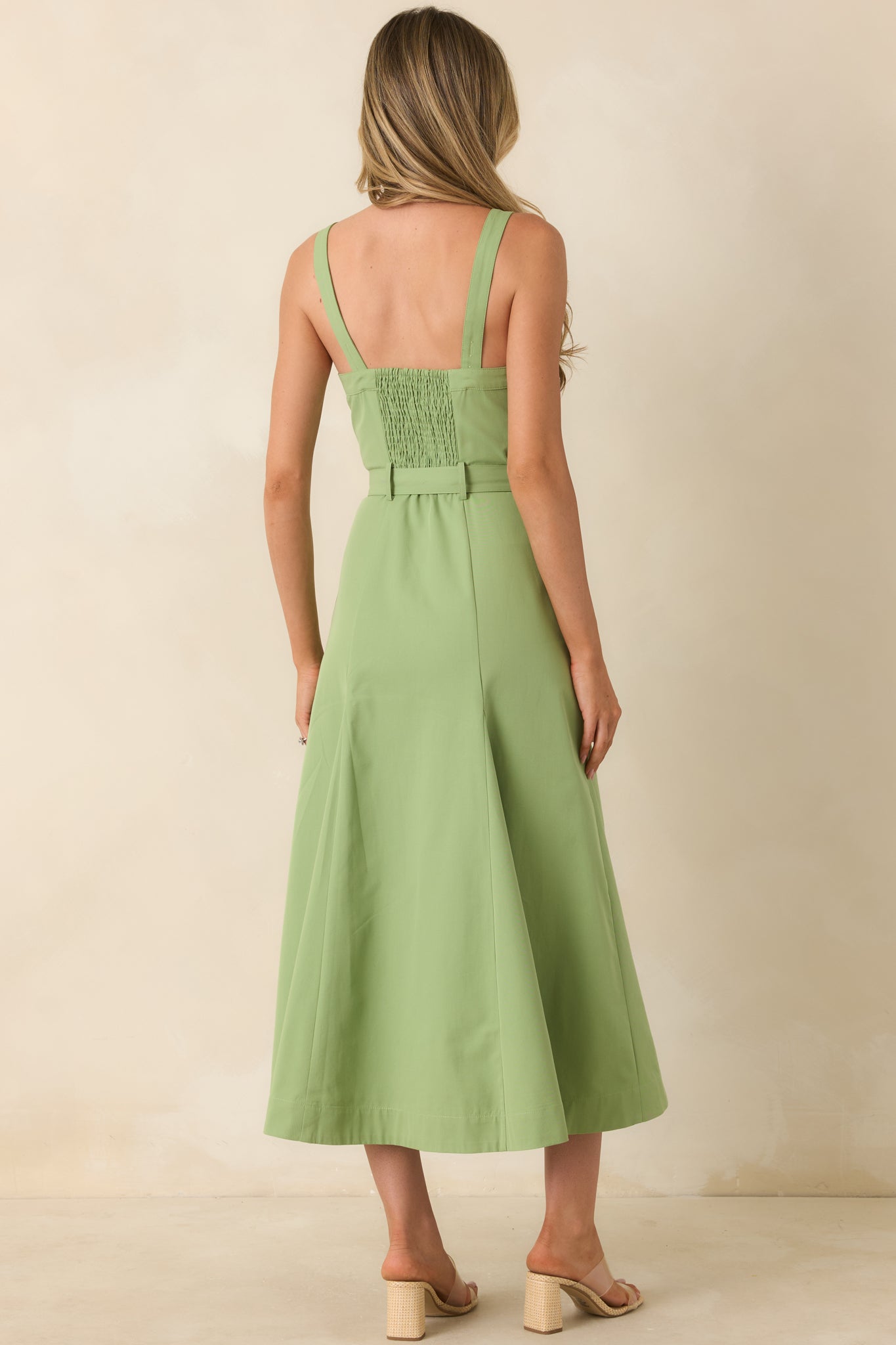Back view of the green midi dress featuring a smocked elastic panel, wide shoulder straps, and a flowing midi-length skirt.