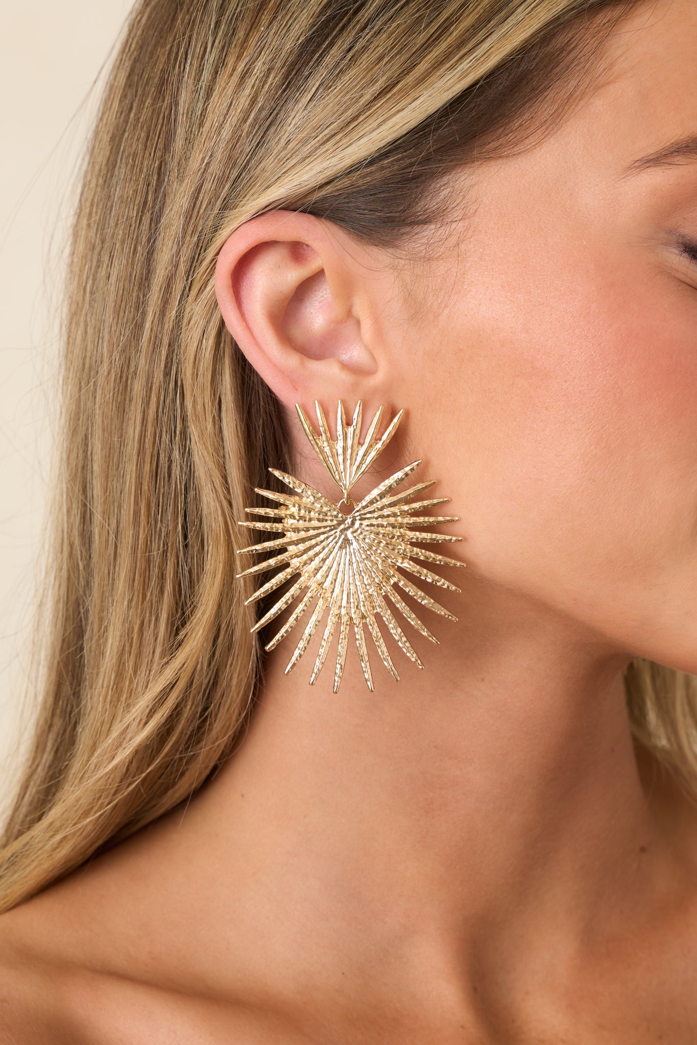 Cropped front view of gold earrings with an intricate, sculptural design and polished finish.