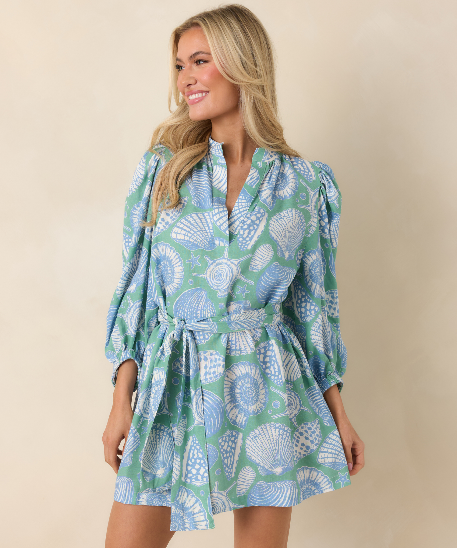 Woman wearing a green and blue sea shell patterned dress on a beige background.