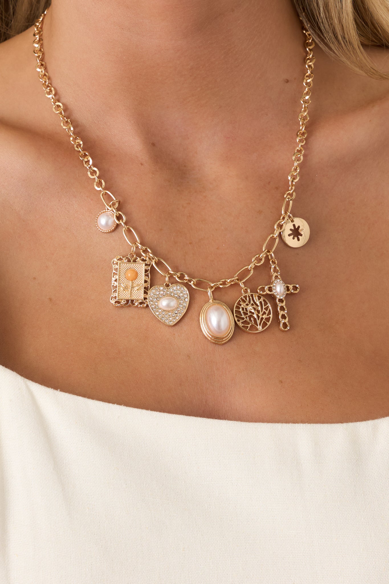 Close-up of gold-tone charm necklace showing pearl, crystal, and link chain details.
