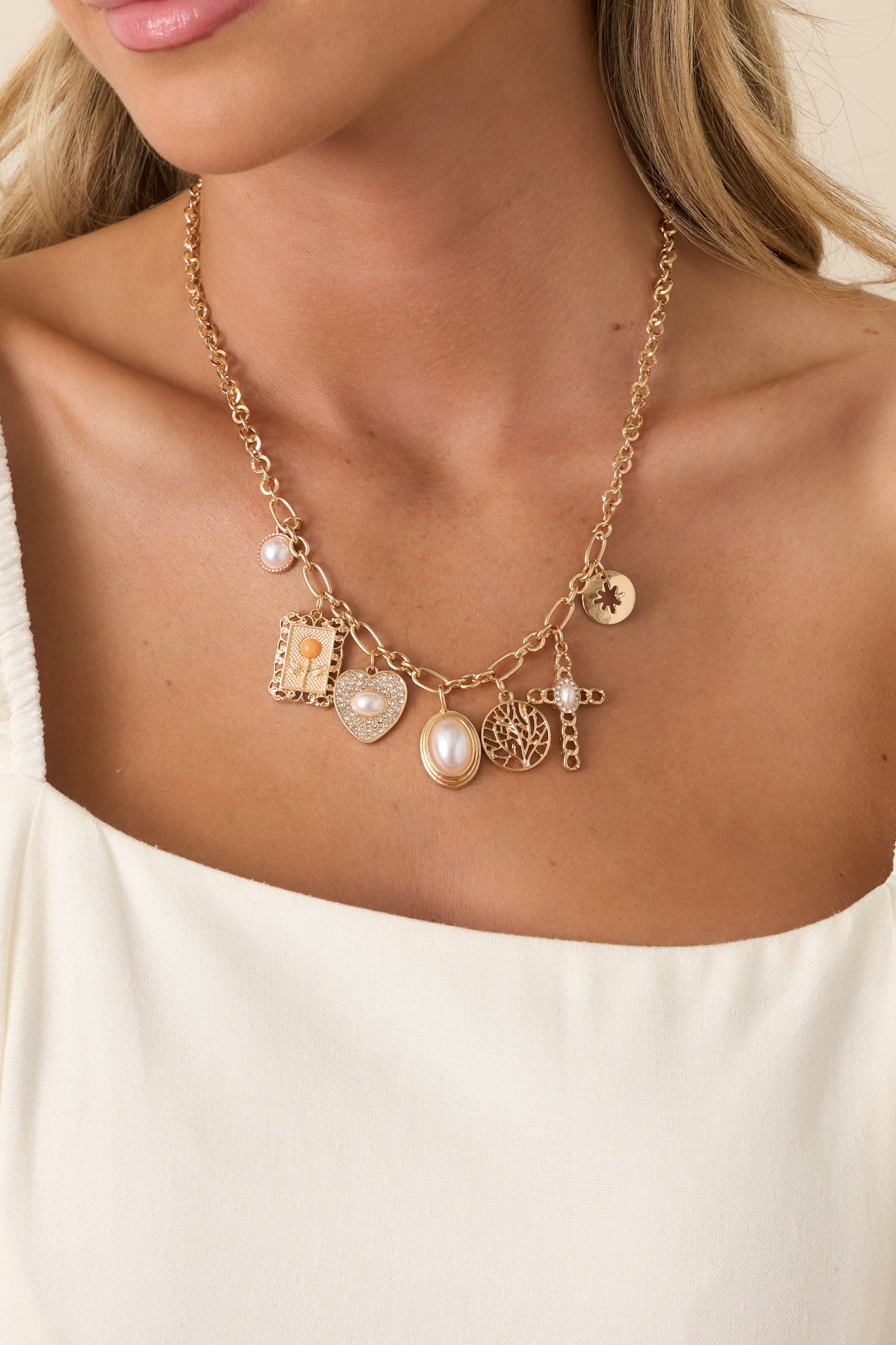Front crop of gold-tone charm necklace featuring mixed pendants with pearl and crystal accents on a link chain.