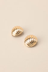 Side view of these earrings that feature gold hardware, a circular shape, a wave-like texture, and secure post backings.