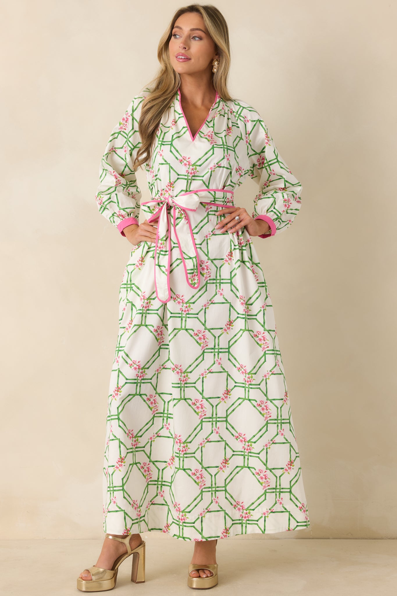 White cotton maxi dress featuring a pink and green floral trellis print, split neckline, and flowing silhouette.
