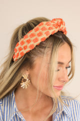 This tan headband features orange, textured polka dots, and a knot at the center.