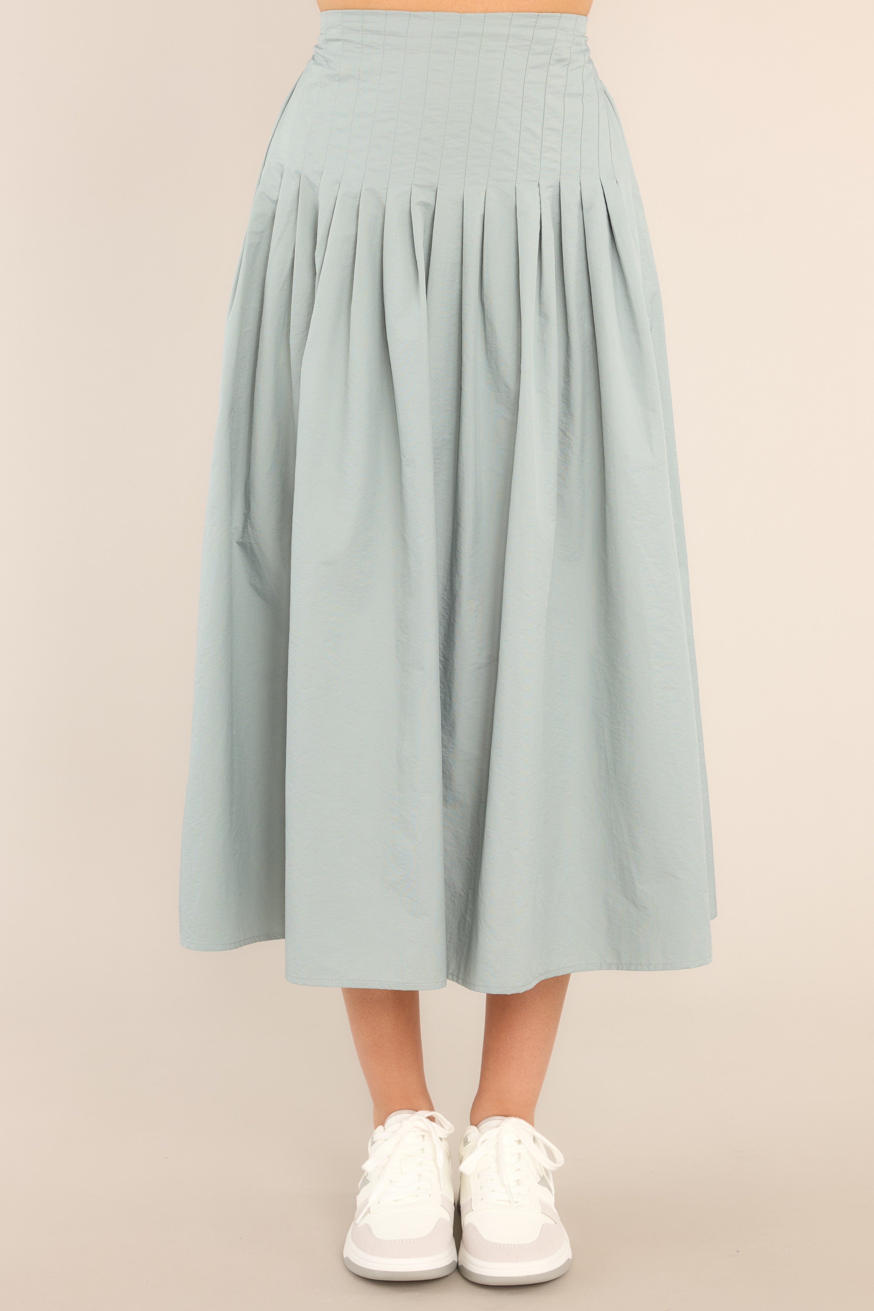Full front view of this skirt that features a high waisted design, an elastic insert at the back of the waist, and intricate pleats around the hipline.