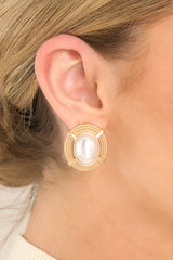 These gold and pearl earrings feature gold hardware, a woven design with an oval shaped faux pearl in the center, and secure post backings. 