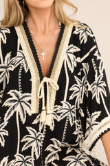 Close up view of this cover up that features a v-neckline with a self-tie feature, crochet detailing, a self-tie belt, a split hemline with self-tie features, and wide sleeves with open knit detailing. 