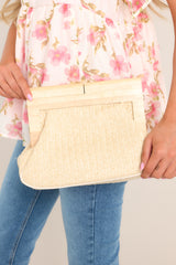 This natural colored clutch features a bamboo handle, a magnetic closure, a small inner pocket, and a removable chain strap.
