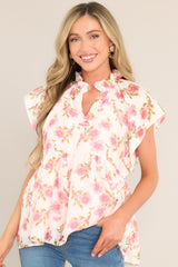 Front view of  this top that features a ruffled v-neckline, a flared waistline, wide transparent sleeves, and a delicate floral pattern.