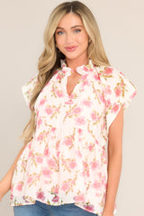 Full front view of  this top that features a ruffled v-neckline, a flared waistline, wide transparent sleeves, and a delicate floral pattern.