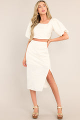 This white skirt features a high waisted design, a discrete side zipper, a thick exposed side seam with ruching, and a side slit.