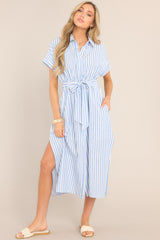 This white and blue dress features a collared neckline, a full button front, a fitted waist, a self-tie waist belt, functional pockets, two side slits, and folded short sleeves.