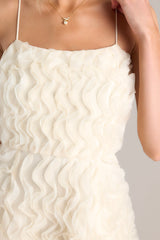 Close up view of this dress that features a rounded neckline, thin straps, and a wavy textured overlay. 