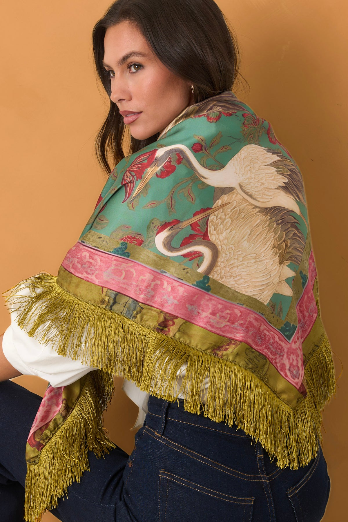 Woman wearing a swan print, fringe scarf in front of a golden backdrop. 