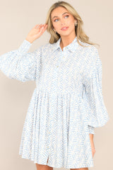 Close up of this blue print dress featuring a collared neckline, functional buttons down the front, long sleeves with smocked cuffs, and a flowy, relaxed fit throughout.