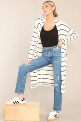 This white and black cardigan features an open-front design, a soft-knit fabric, functional pockets, and long sleeves.