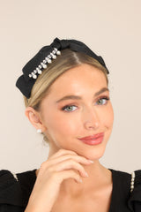 This black headband features a cloth covered metal piece, a black bow attached to the top, a thin body, diamond & pearl detailing, and rubber tips.