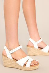 These white sandals feature a rounded toe, straps over the top of the foot and around the ankle, a buckle closure, and a natural wedged heel. 