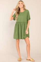 This sap green dress features a round neckline, a keyhole cutout at the back of the neck with a button closure, short sleeves, ruffle detailing along the waistline, and functional pockets at the hips. 
