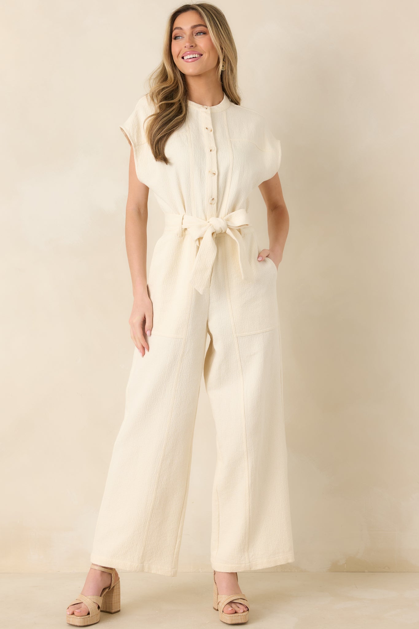 Jumpsuit with subtle cap sleeves, side pockets, and flowing wide-leg design, shown front-facing.