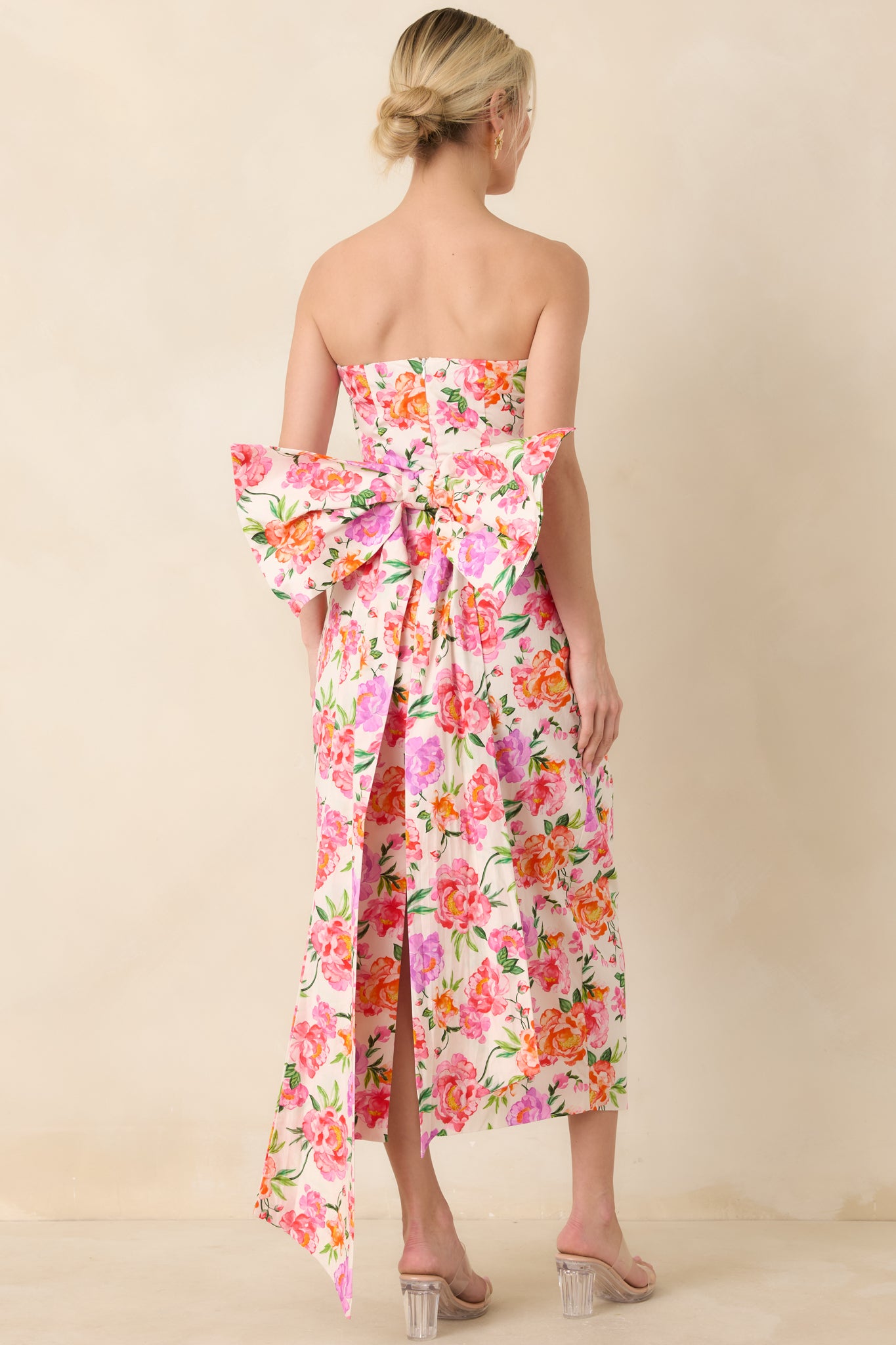 Rear view of the strapless pink midi dress showcasing the oversized bow cascading down the back and the elegant skirt flow.