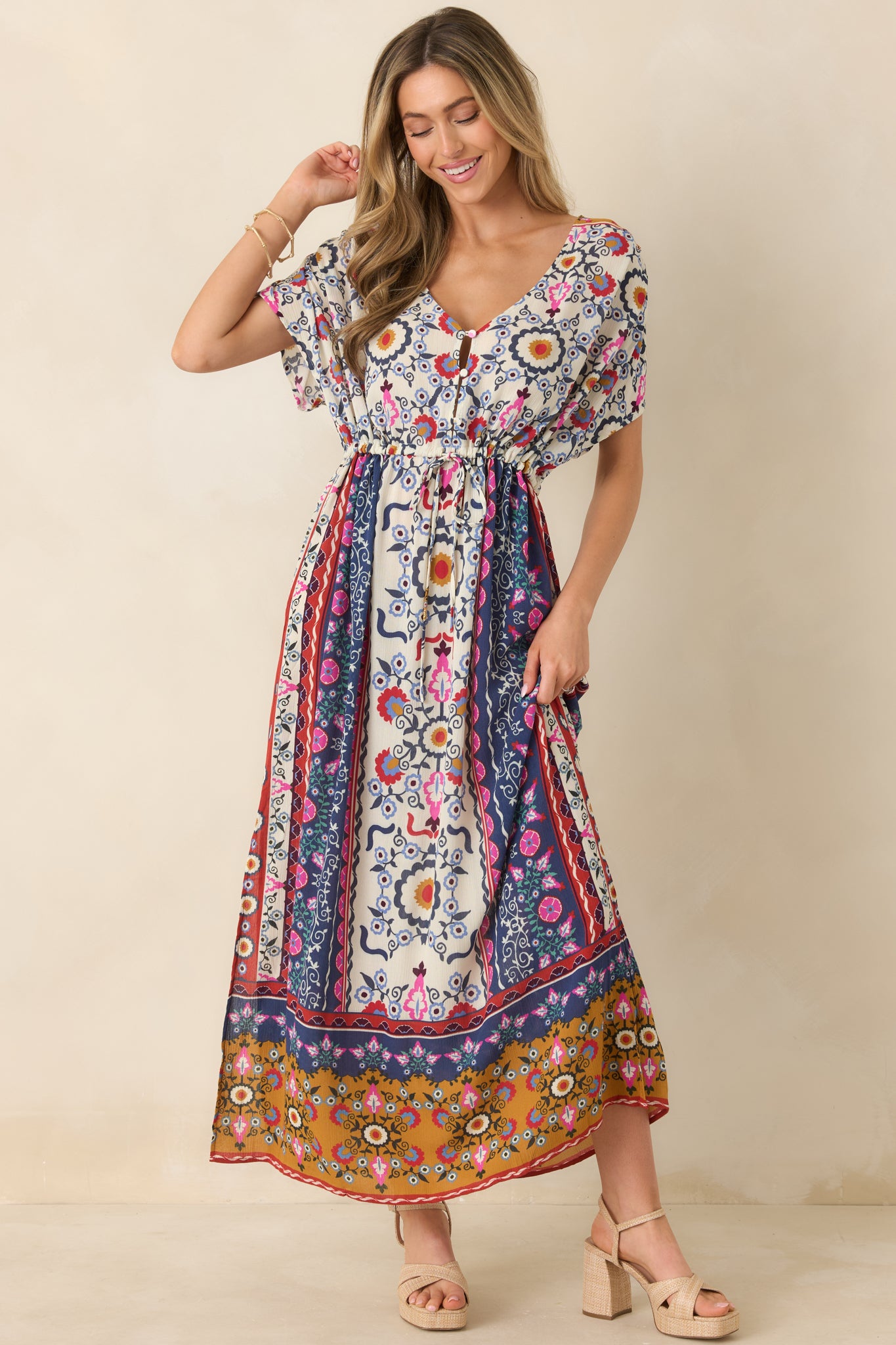 Woman wearing a colorful floral, maxi dress against a beige background.