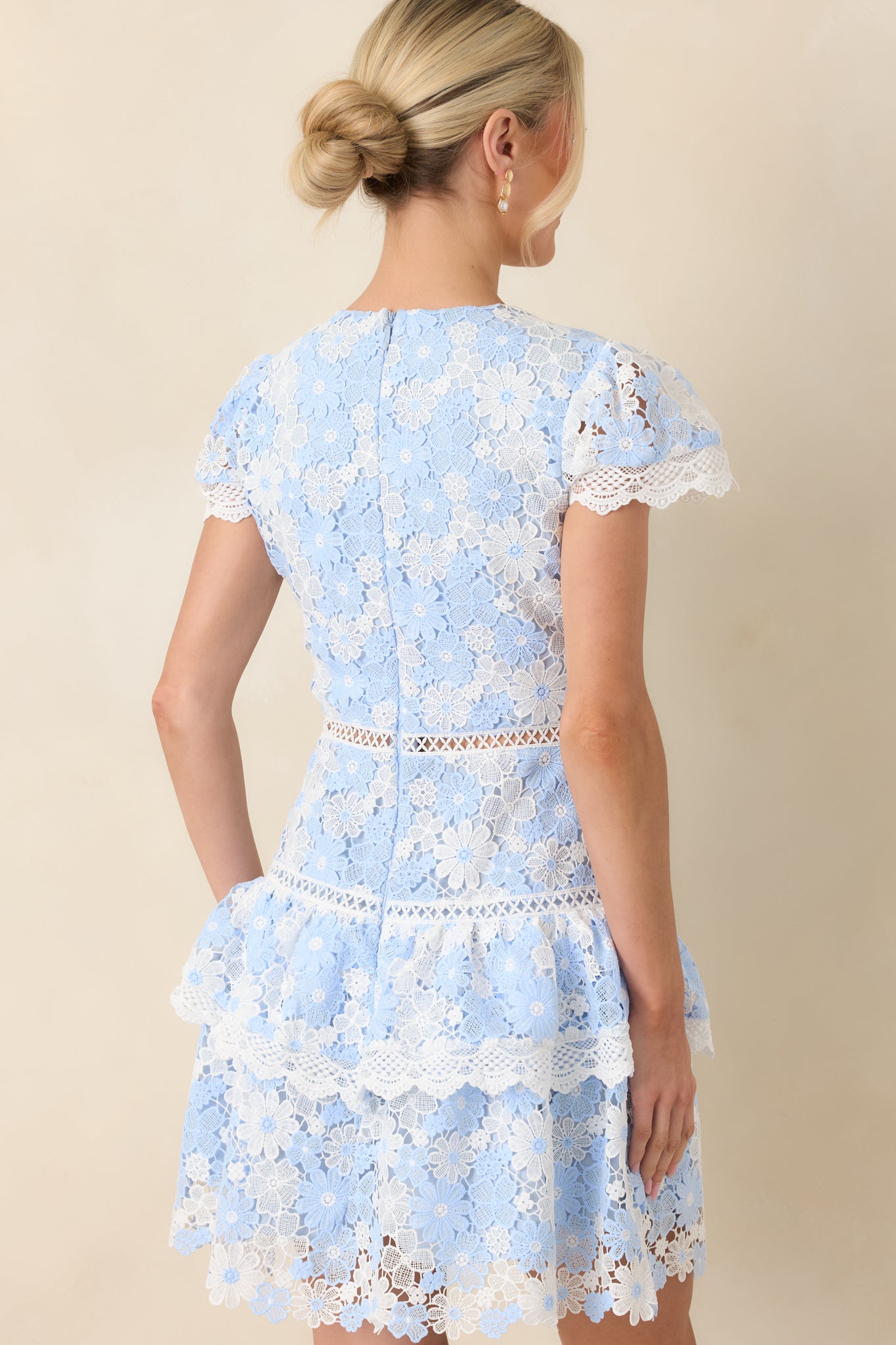 Rear view of the blue and ivory lace mini dress highlighting the intricate overlay and tiered ruffle hem from behind.