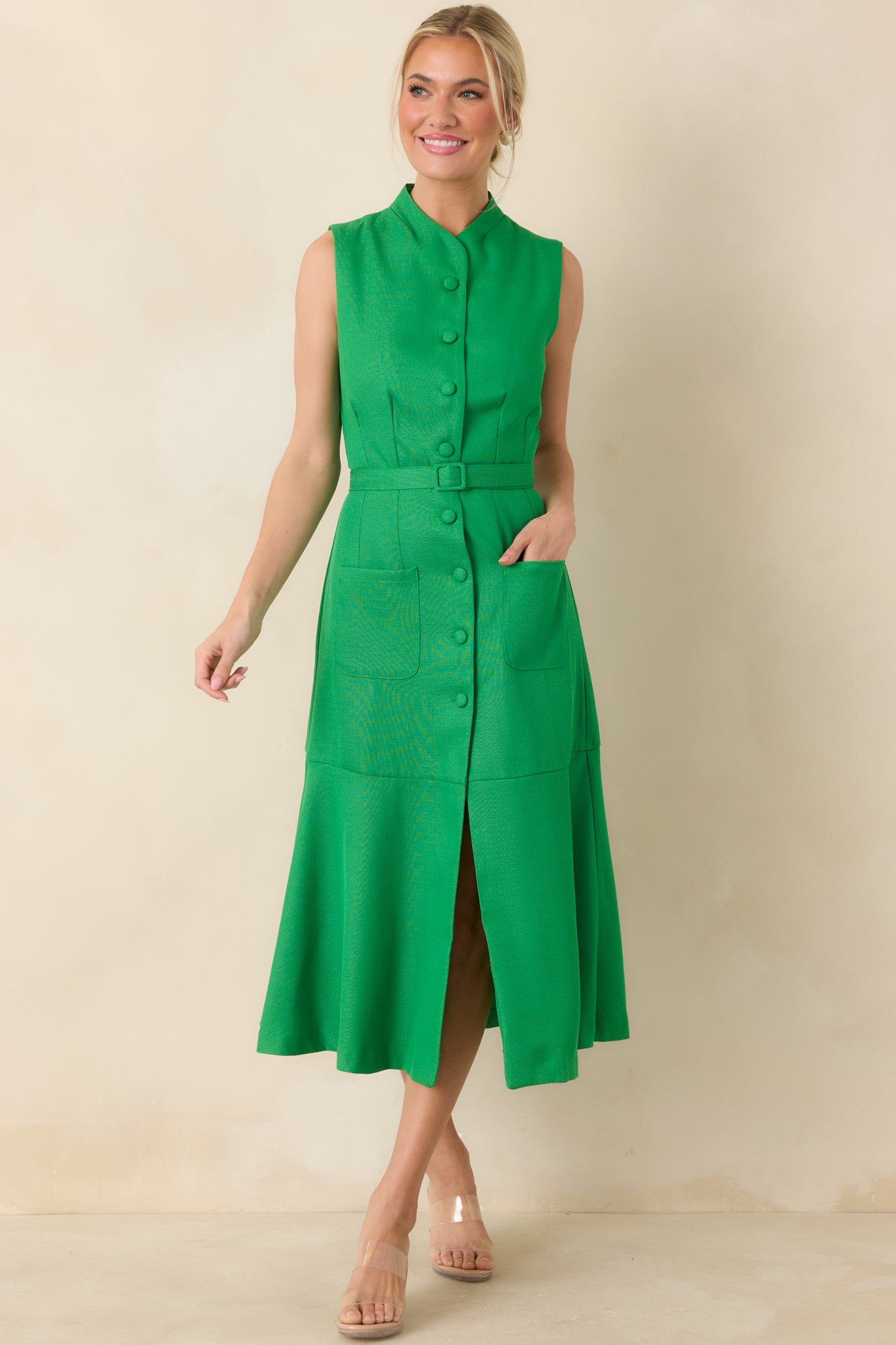 Structured green midi with clean lines, stand collar neckline, covered buttons down the front, defined waist belt, patch pockets, and a graceful flared skirt.