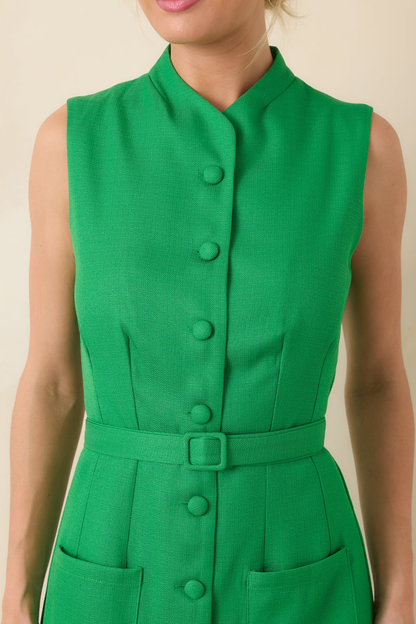 Detailed view of the vivid green fabric highlighting the stand collar, covered buttons, vertical seam detailing, and the coordinating belt with patch pocket accents.