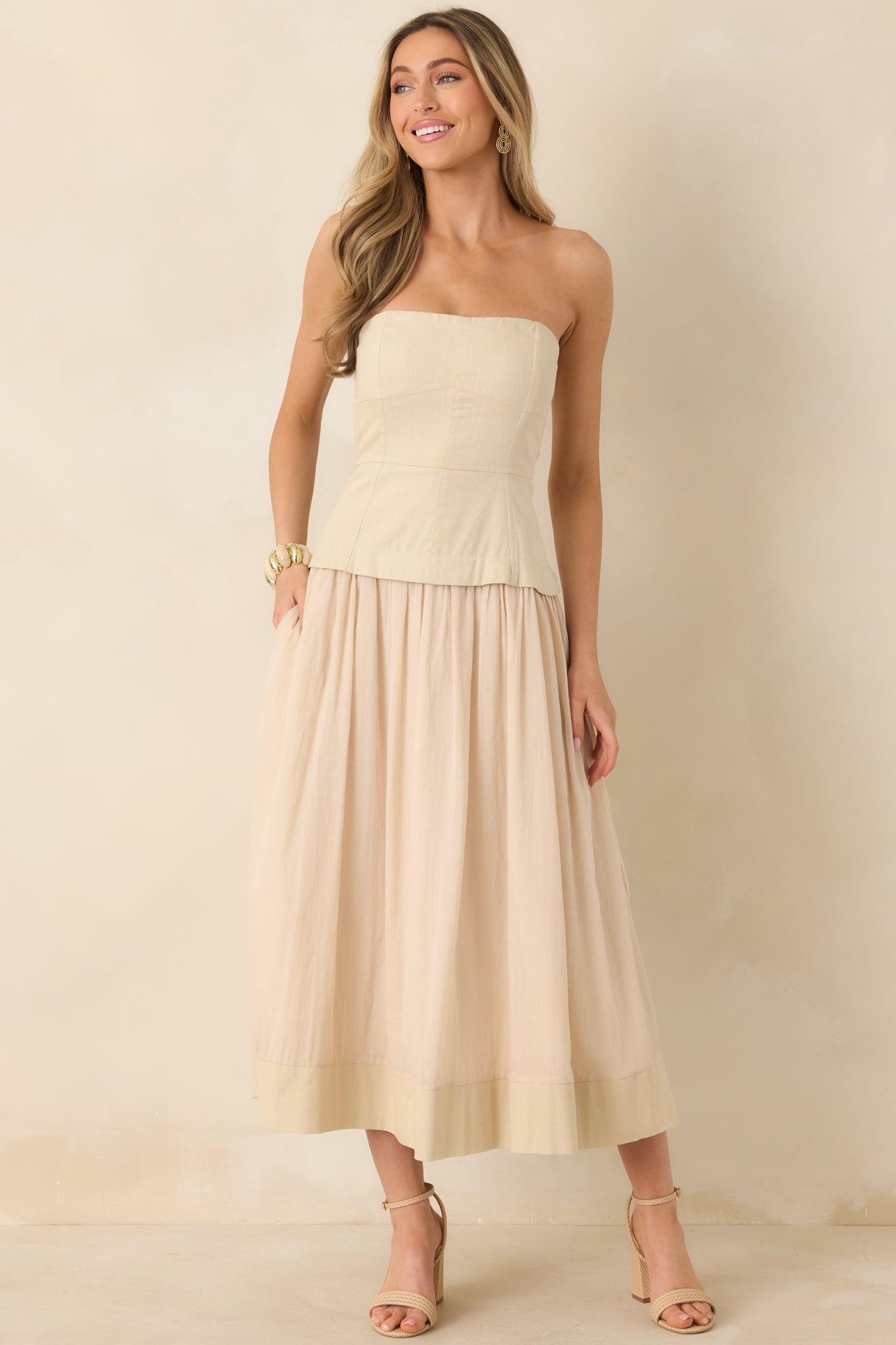 Beige midi dress with bustier-style paneled bodice, adjustable spaghetti straps, and flowy gathered skirt.