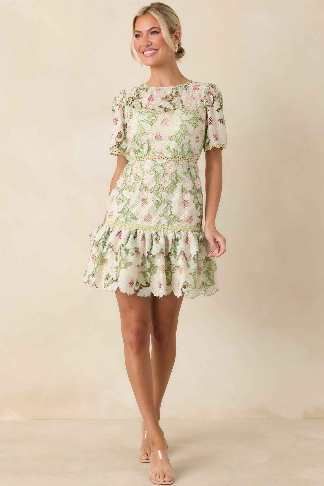 Green lace mini dress layered over a coordinating lining, featuring soft pink floral accents and a flounced ruffle hem.