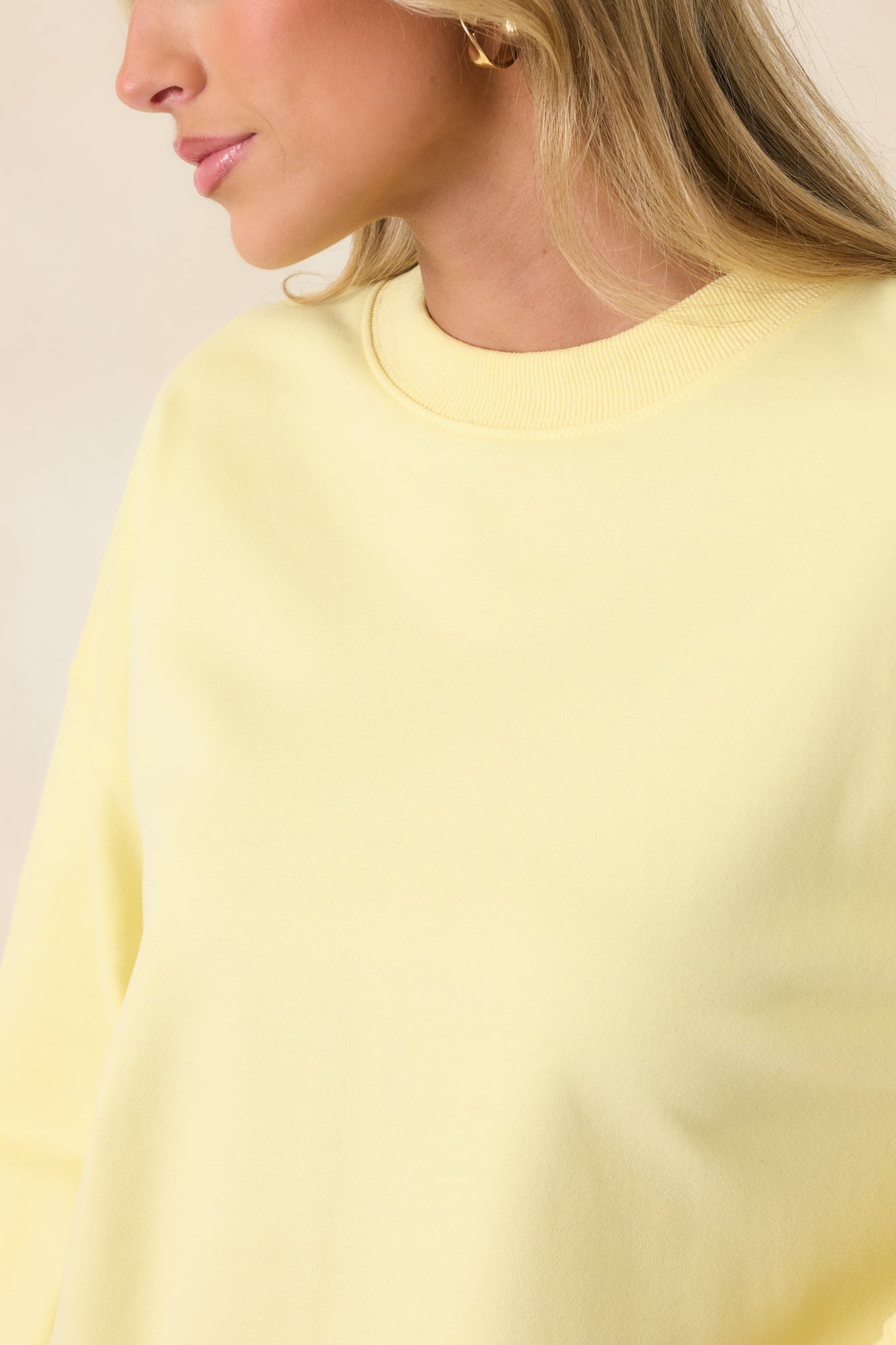Close-up of yellow sweatshirt fabric showing ribbed trim, crew neckline, and soft knit texture.