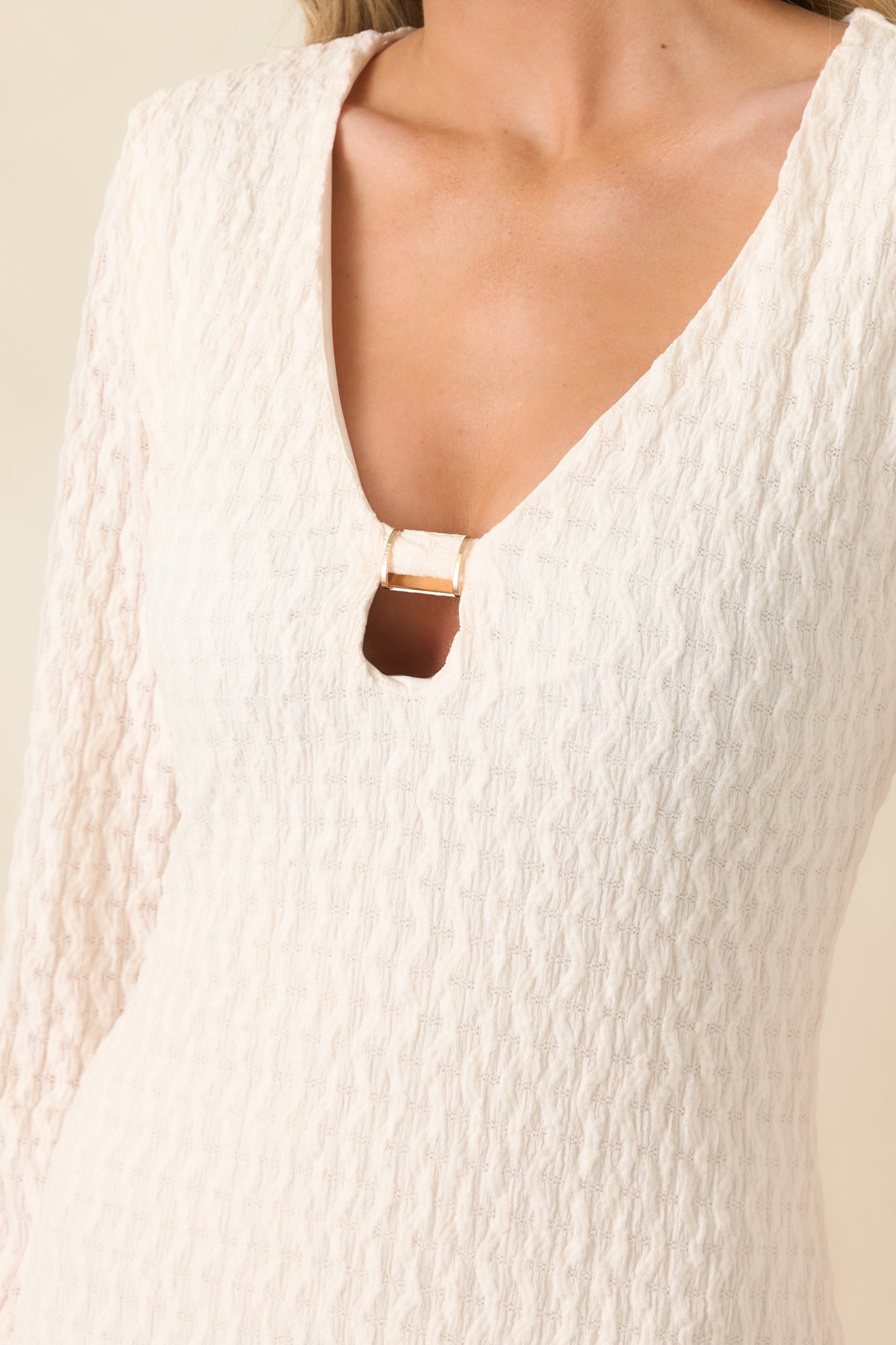 Close-up of textured, semi-sheer fabric with gold-tone neckline accent.