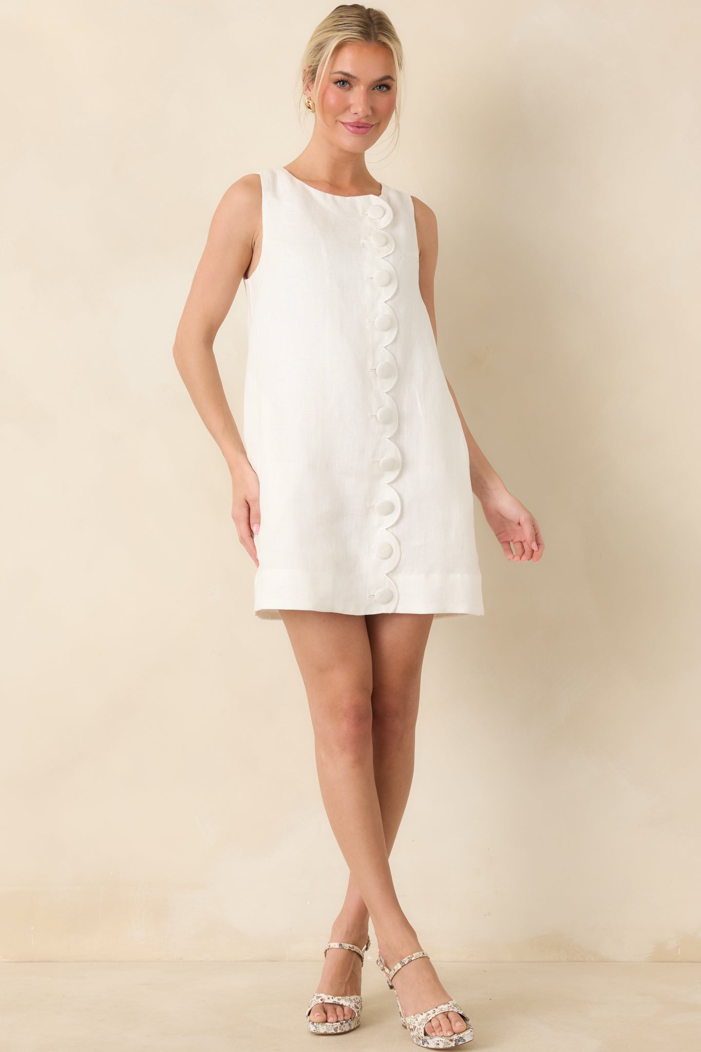 Crisp, white shift mini dress featuring scalloped trim and covered button accents.