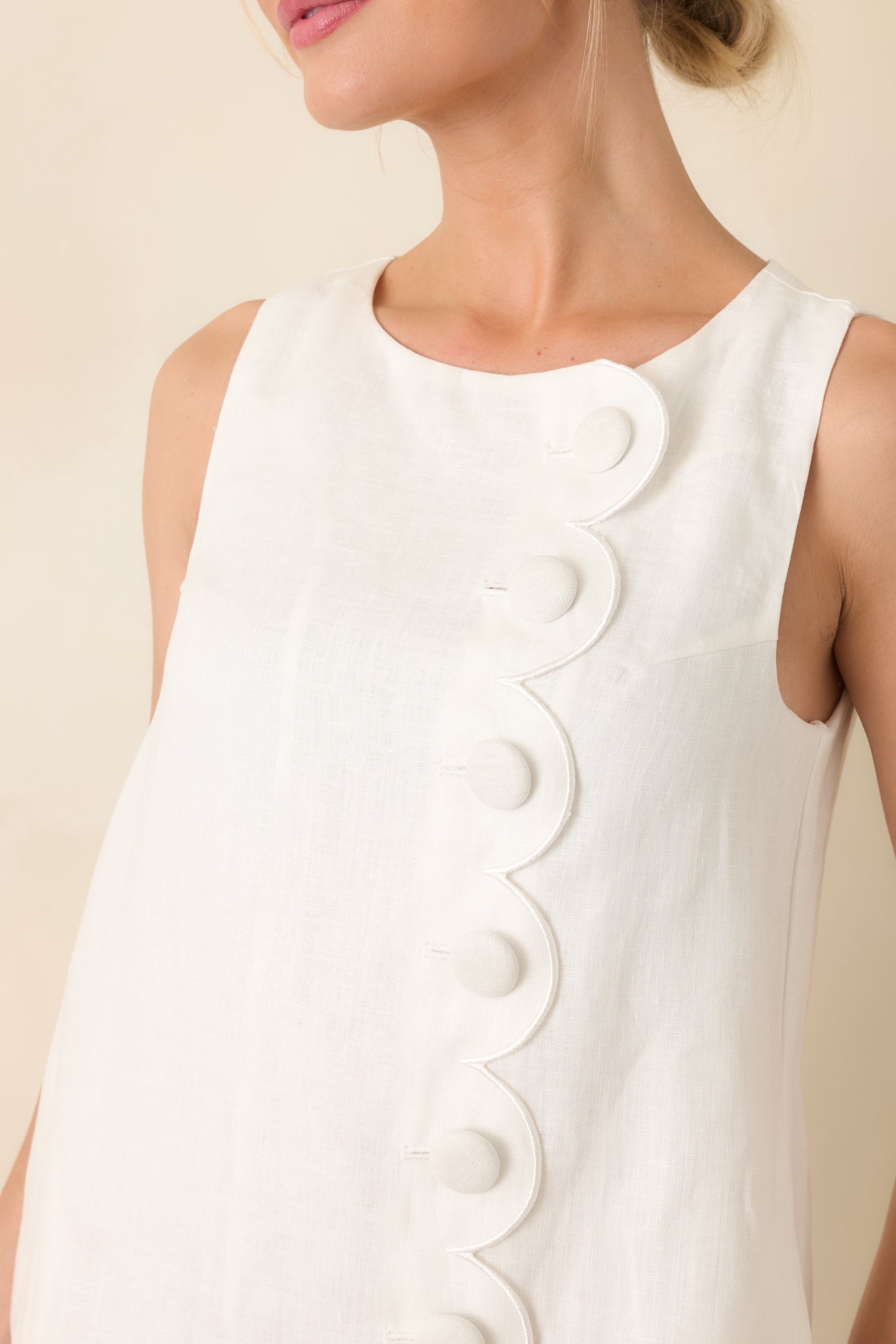 Close-up of scalloped panel with covered button detailing on white fabric.