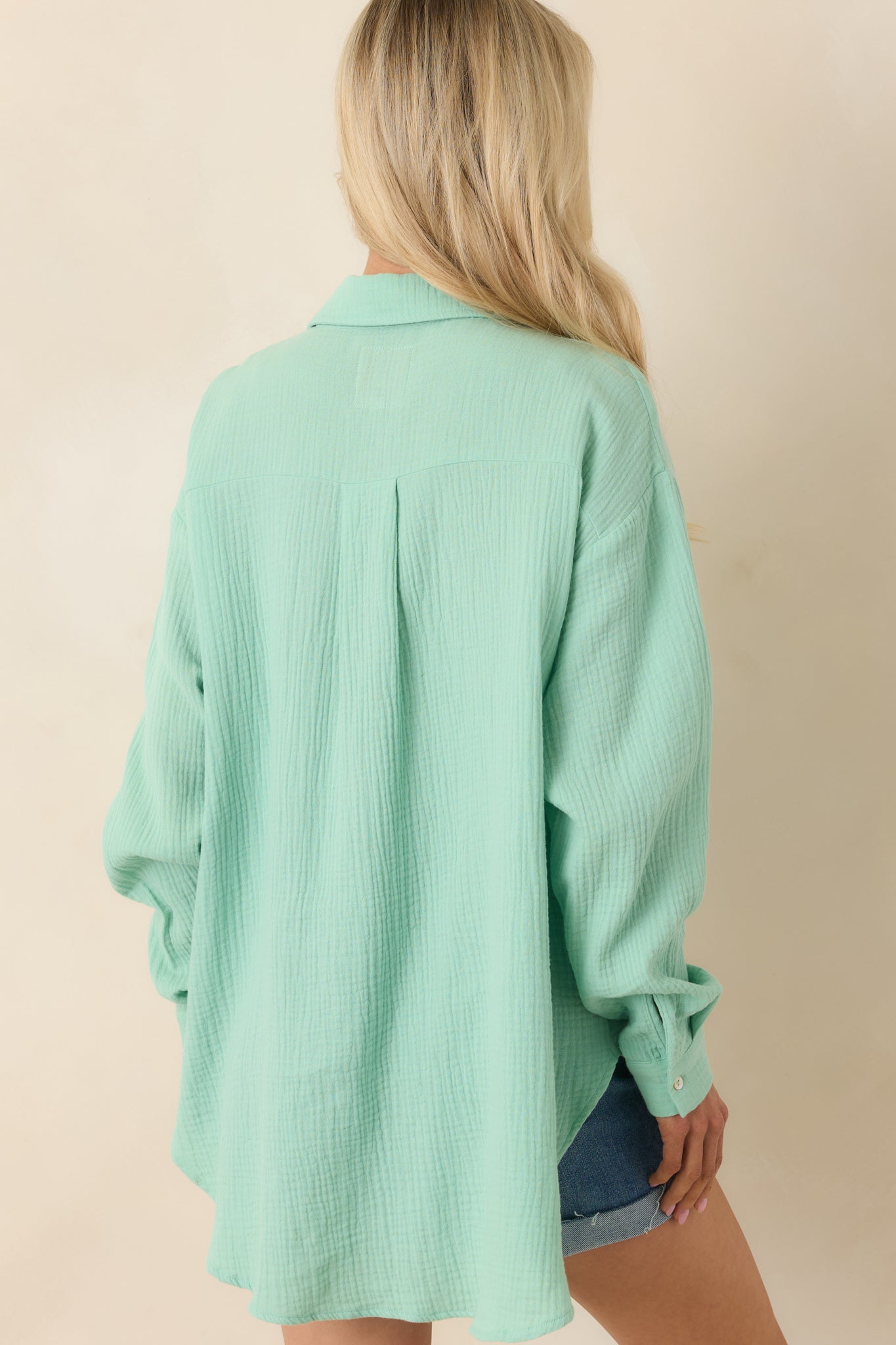 Rear view of light green button-up top featuring relaxed silhouette and extended high-low hemline.