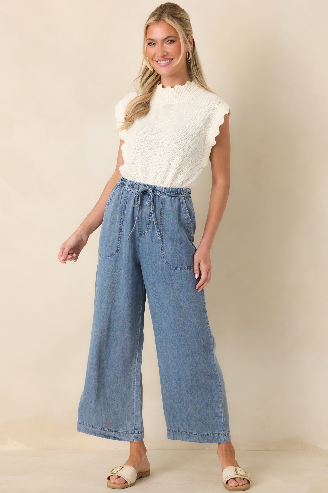 Front view of a white sleeveless sweater with textured knit, ribbed mock neckline, and scalloped shoulder edges.