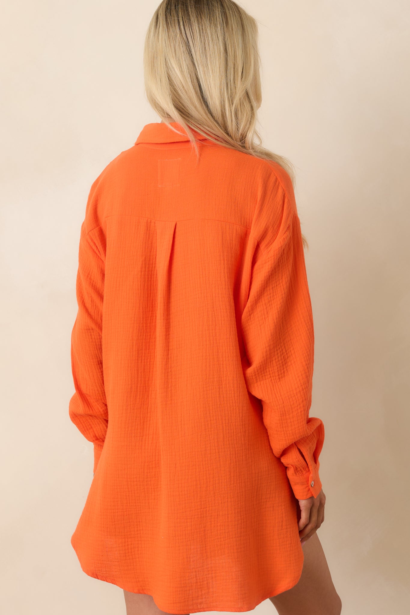 Rear view of the orange cotton button-up with relaxed silhouette, long sleeves, and high-low hemline.