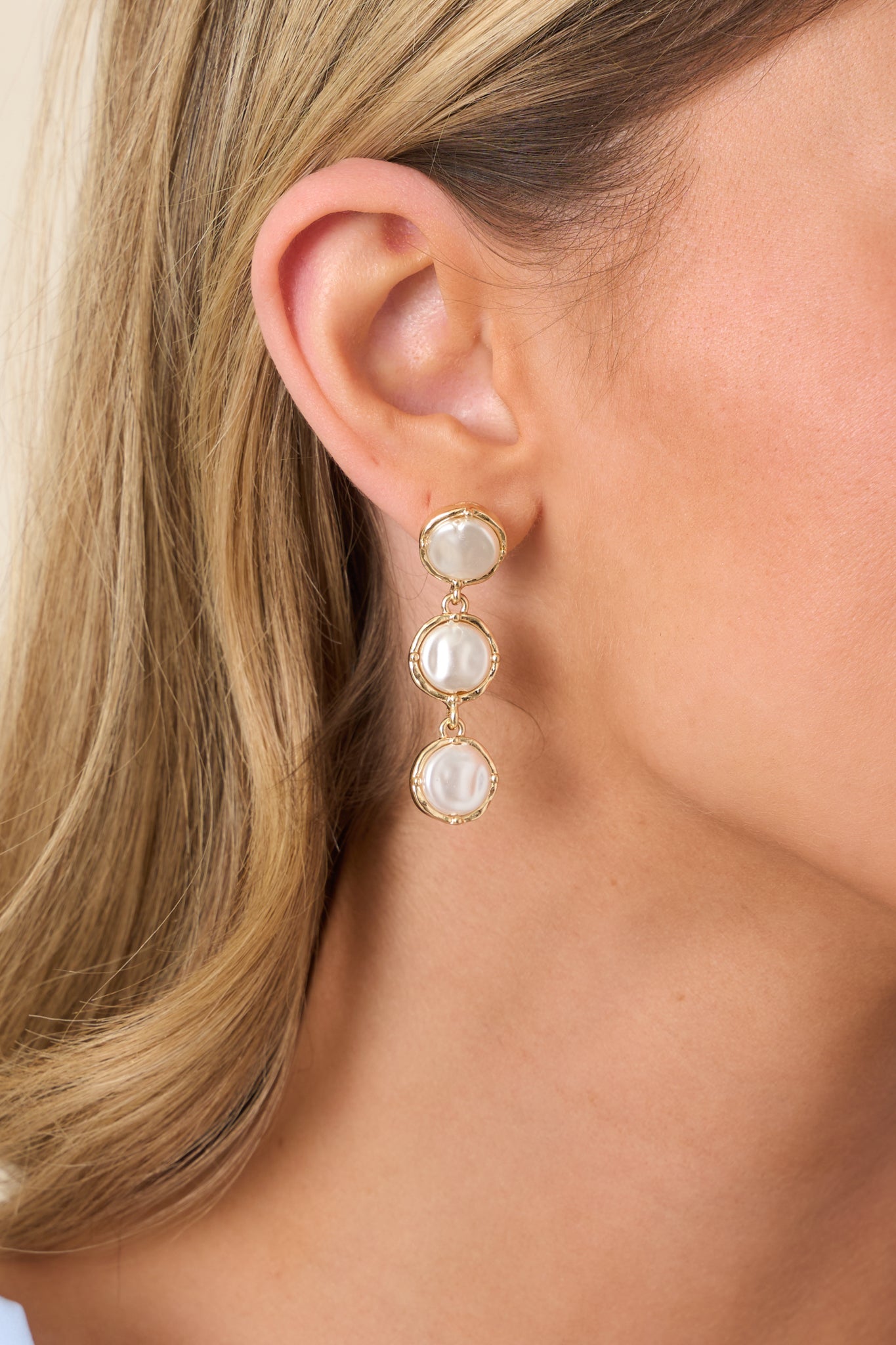 Close-up of three luminous pearls and polished gold setting on statement tiered drop earrings.