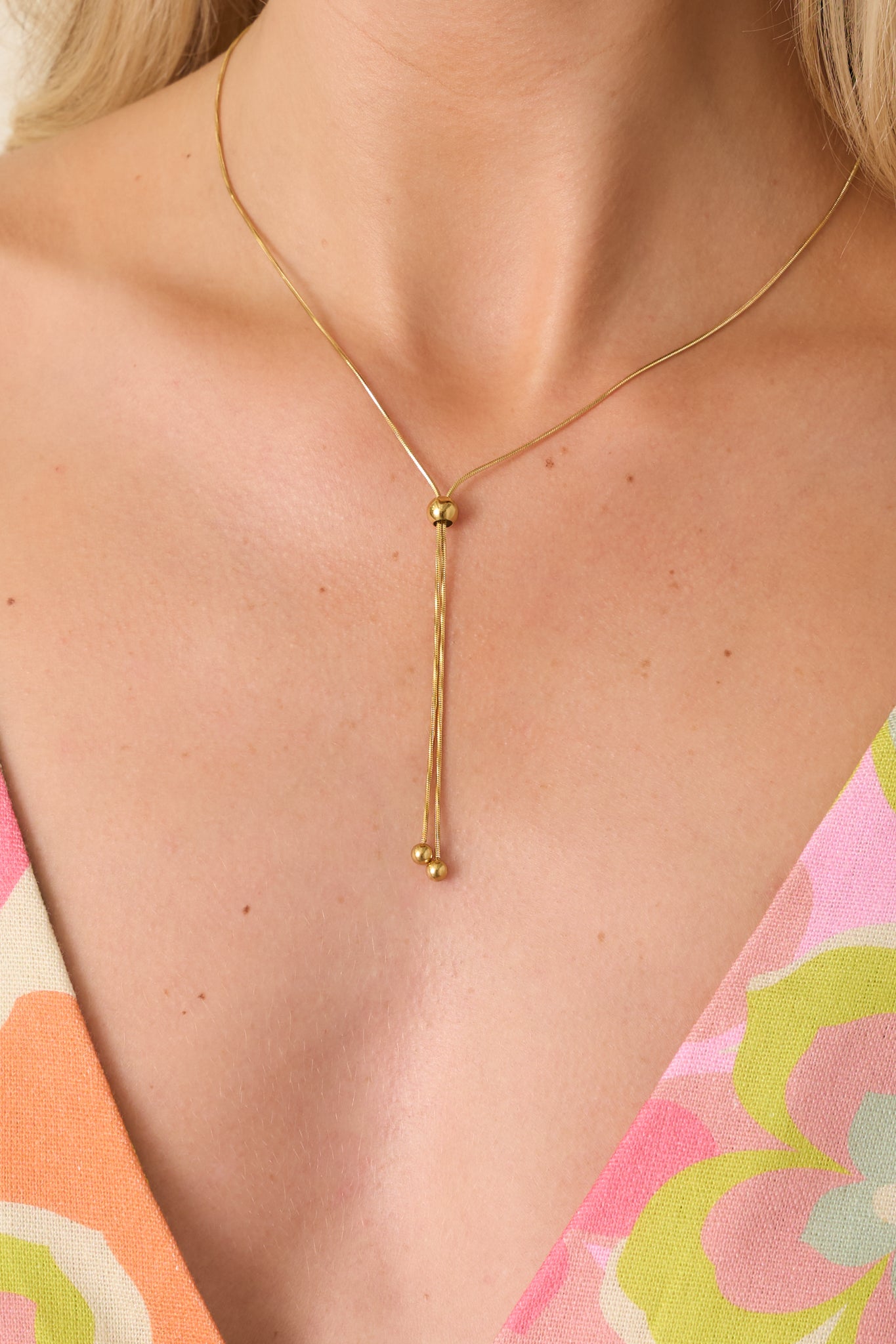 Close-up of gold lariat necklace highlighting the fine chain, adjustable sliding bead, and drop detail.