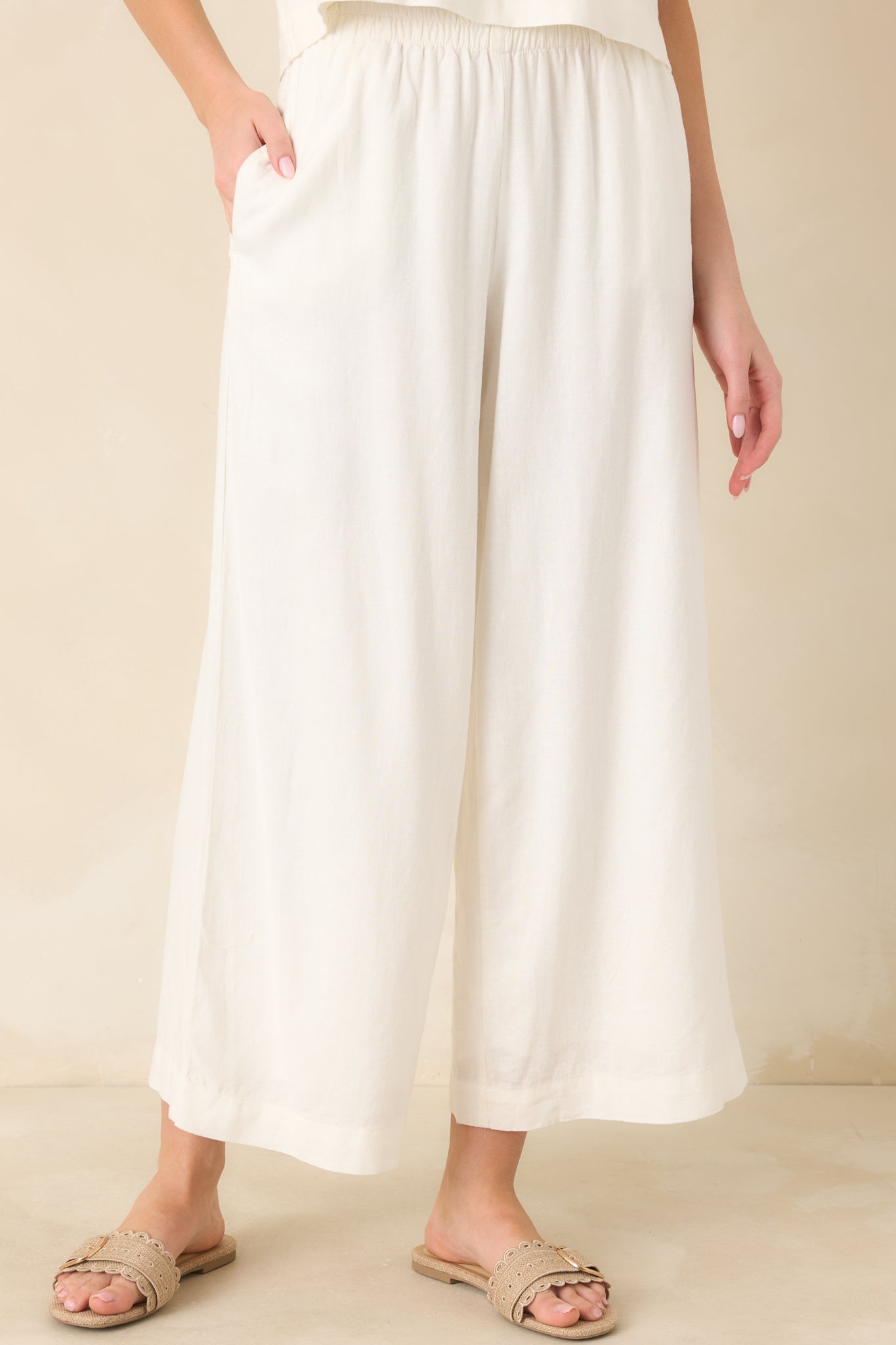 White linen pants highlighting the comfortable elastic waistband and softly structured wide-leg shape with subtle texture throughout.