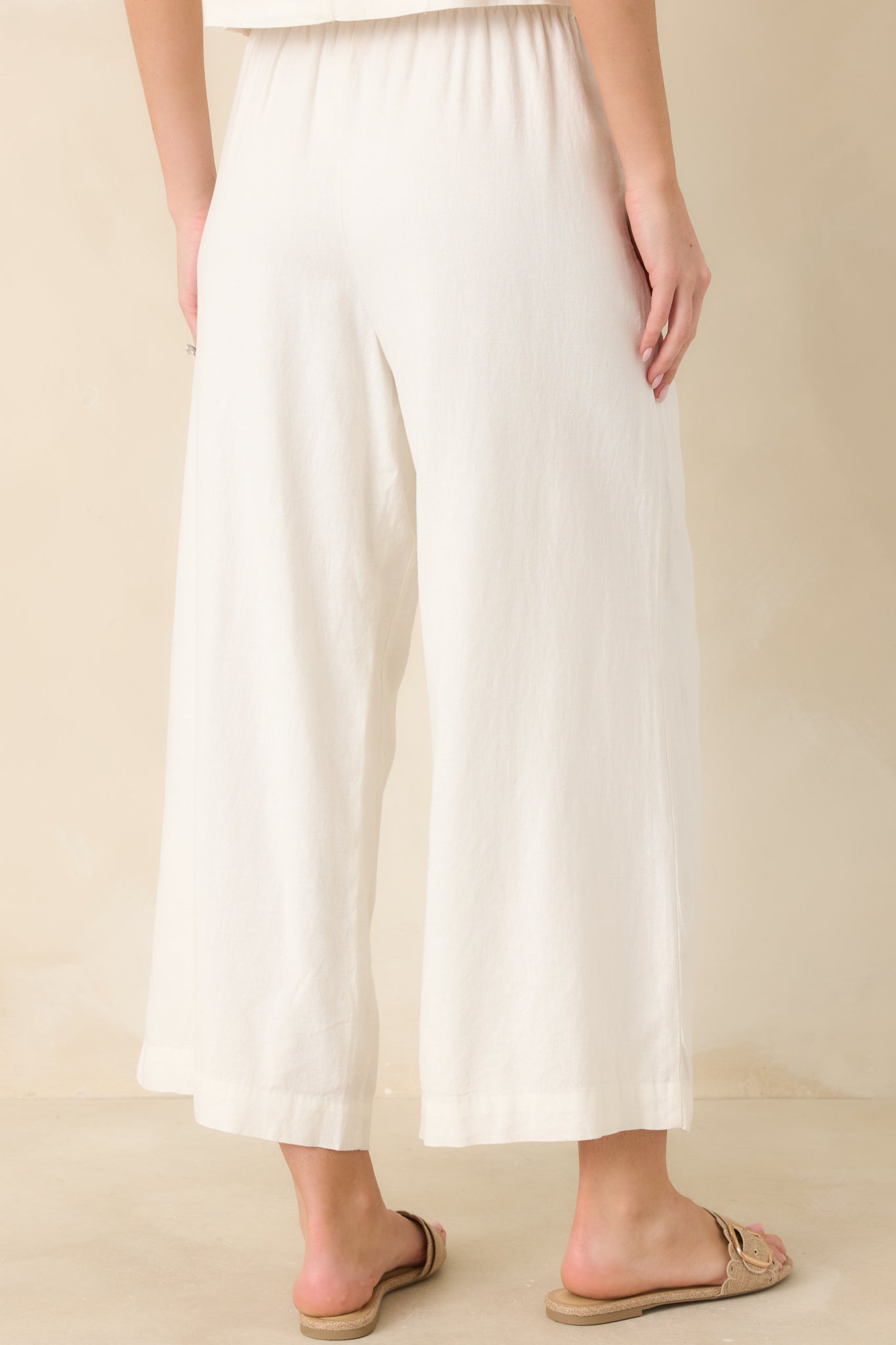 Rear view of white linen wide-leg pants featuring the relaxed ankle-length cut and comfortable elastic waistband for an easy, breathable fit.