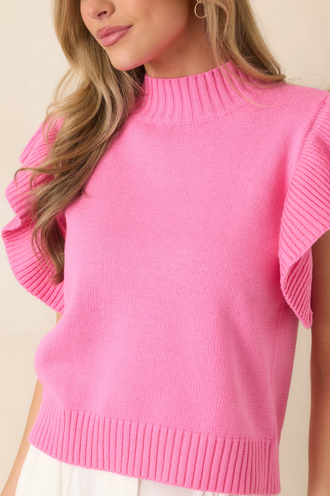 Close view of hot pink knit fabric showing ribbed mock neckline, flutter sleeve texture, and ribbed hem finish.